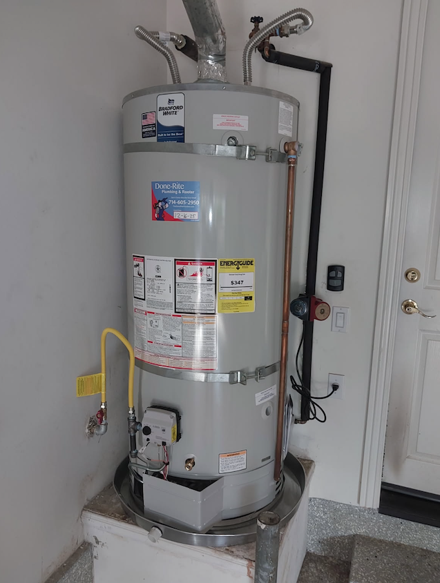 Water heater with pipes and valves in a utility closet, shown against a wall beside a door.