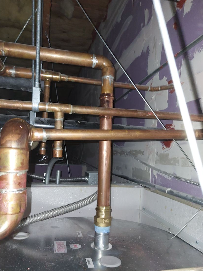 Copper pipes and gray insulation in a utility space with exposed plumbing and wiring