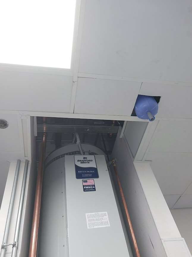 Water heater in ceiling alcove with a damaged opening and a blue pipe protruding nearby.