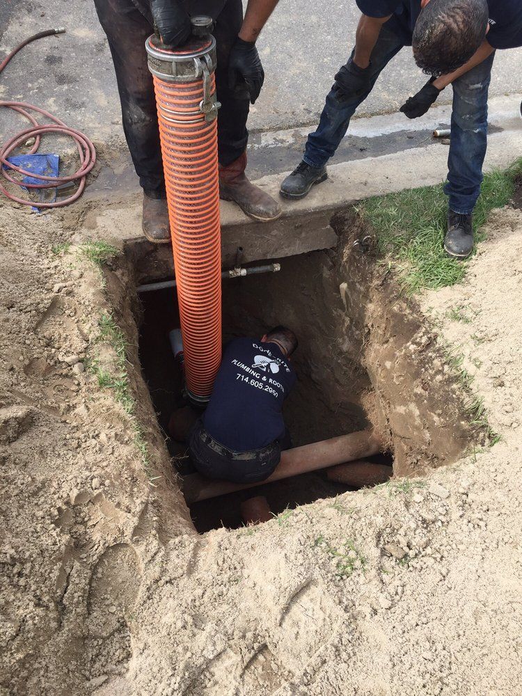 Workers in a trench using an orange hose to inspect or repair underground pipes
