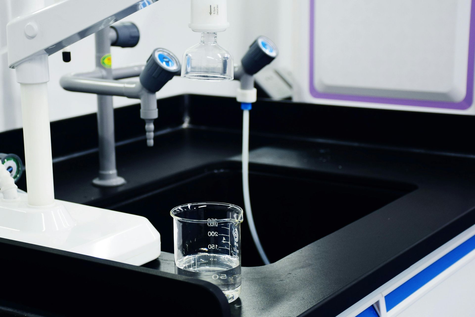 Lab sink with faucets and a beaker in a black basin