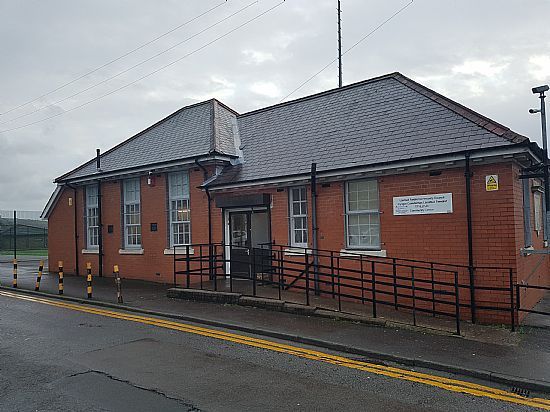 Red brick building with a ramp, windows, and a black railing under a gray sky.