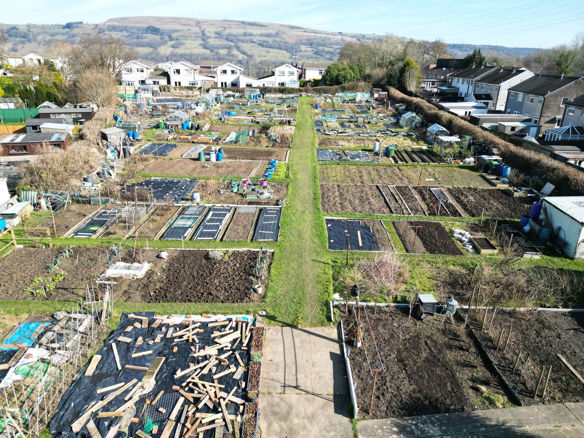 Aerial view of an allotment with many plots; some covered in mulch, others planted. Paths run between the plots.