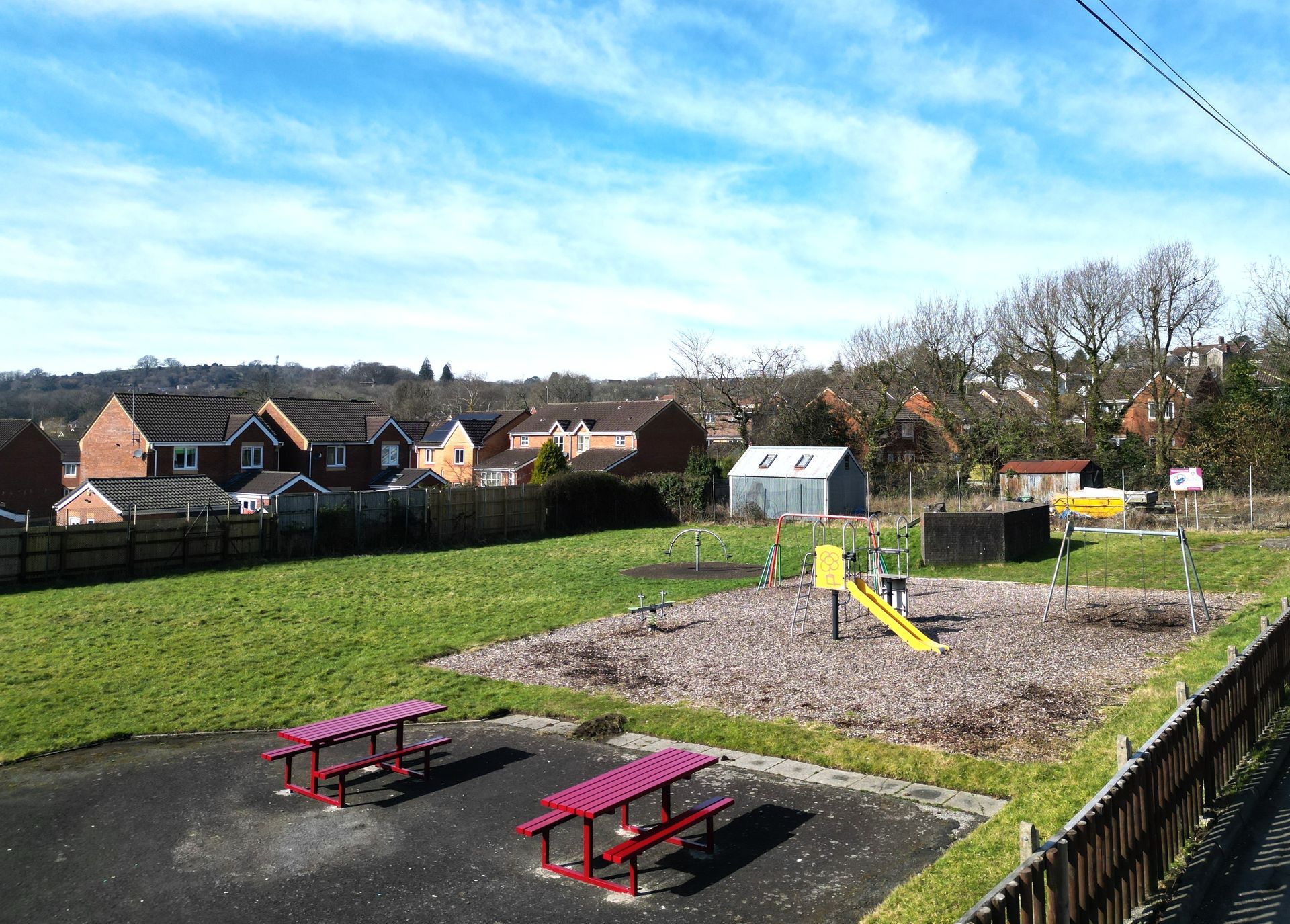 Playground with slides, swings, and picnic tables on a sunny day with houses in the background.