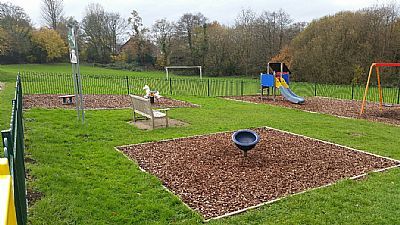 Playground with swing set, slide, and bench, surrounded by grass and trees.