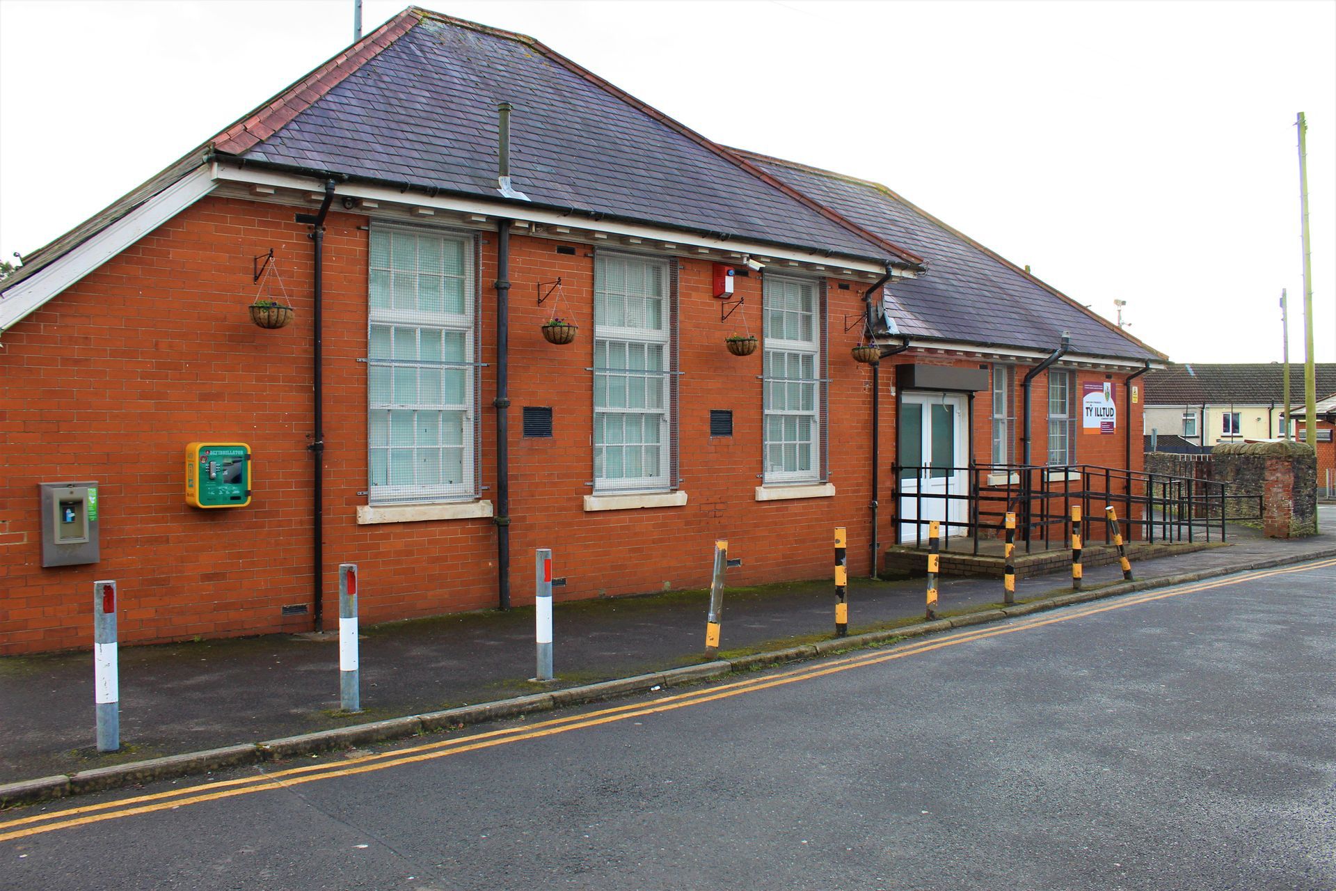Red brick building, likely a post office, with white-framed windows, phone box, and a covered entrance.