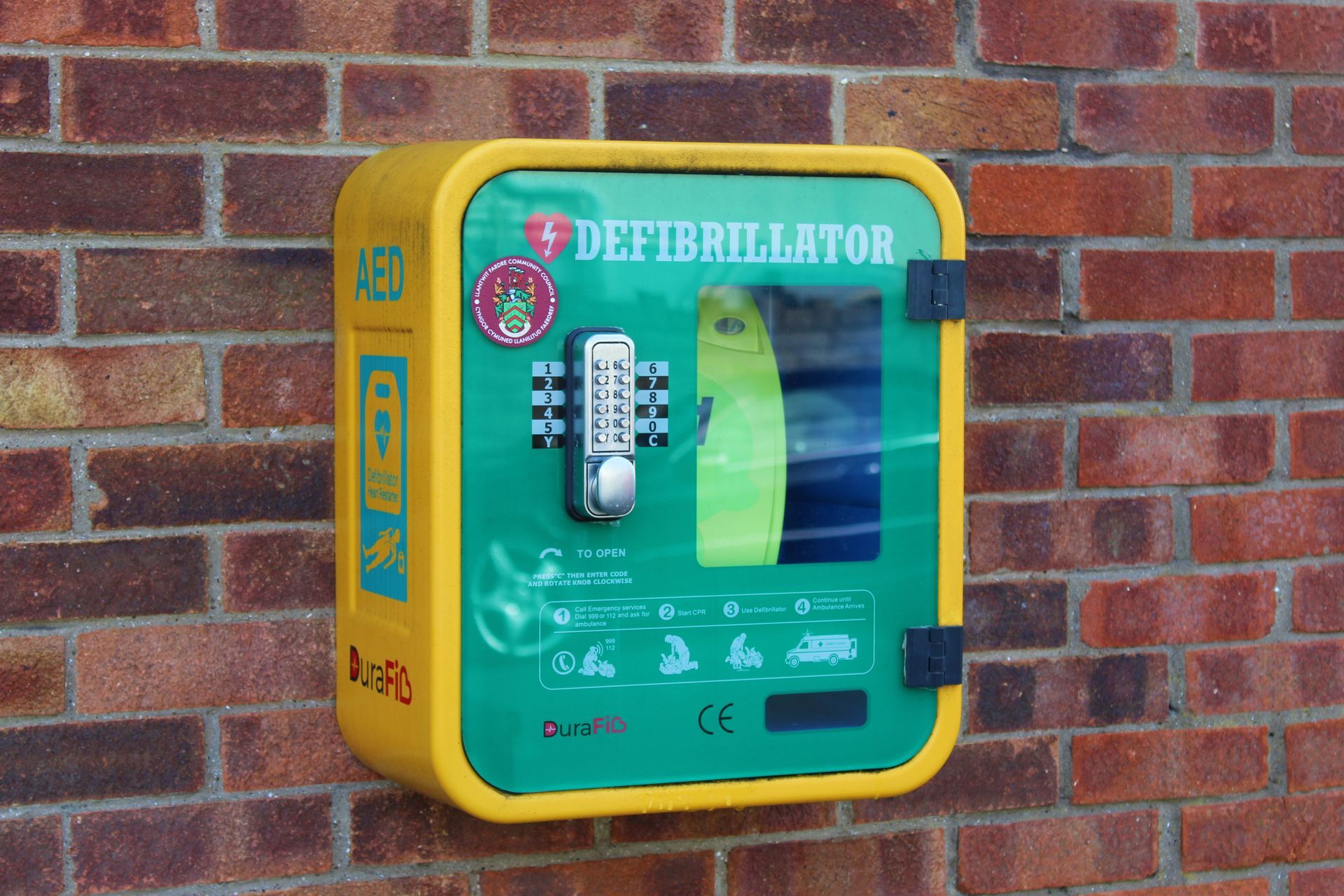 Yellow and green AED (automated external defibrillator) case mounted on a brick wall.