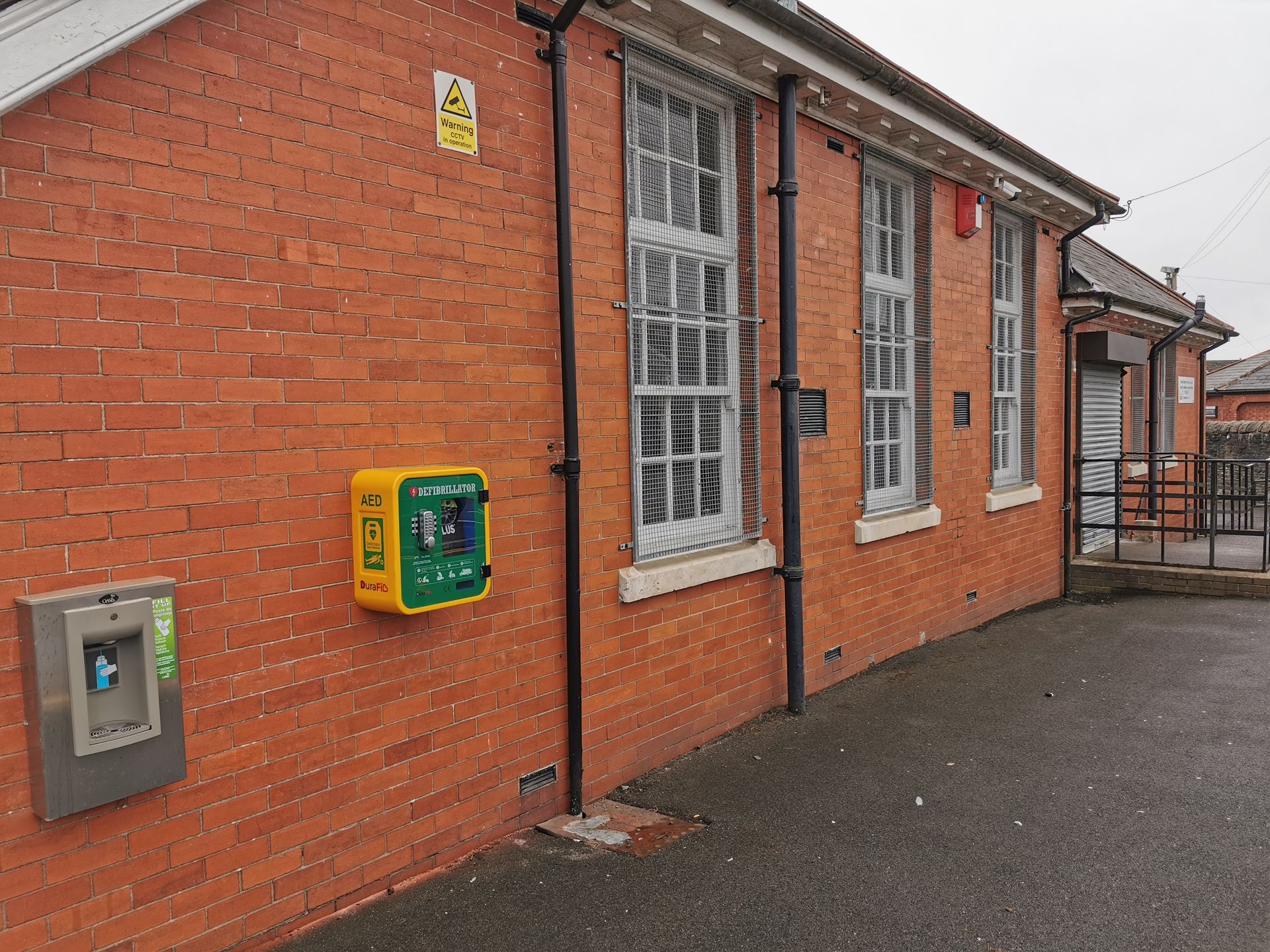 Exterior of a brick building with a bright yellow AED and a water fountain mounted on the wall.
