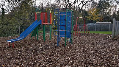 Playground with blue slide, climbing structure, and monkey bars, covered in wood chips.