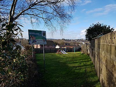 Grassy backyard with a sign, a slide, and a distant town, under a bright, cloudy sky.