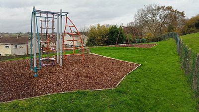 Playground with climbing frames, swings, and grassy hill on a cloudy day.