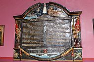 Memorial plaque on pink wall, names inscribed, architectural details top and bottom, two flag-bearing figures on either side.