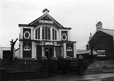 A brick building with arched windows, possibly a church, with a decorative facade and dark fence.