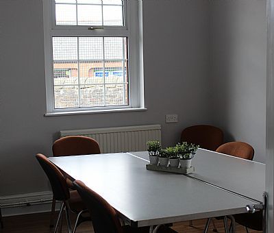 A small meeting room with a white table and brown chairs, window, and plants.
