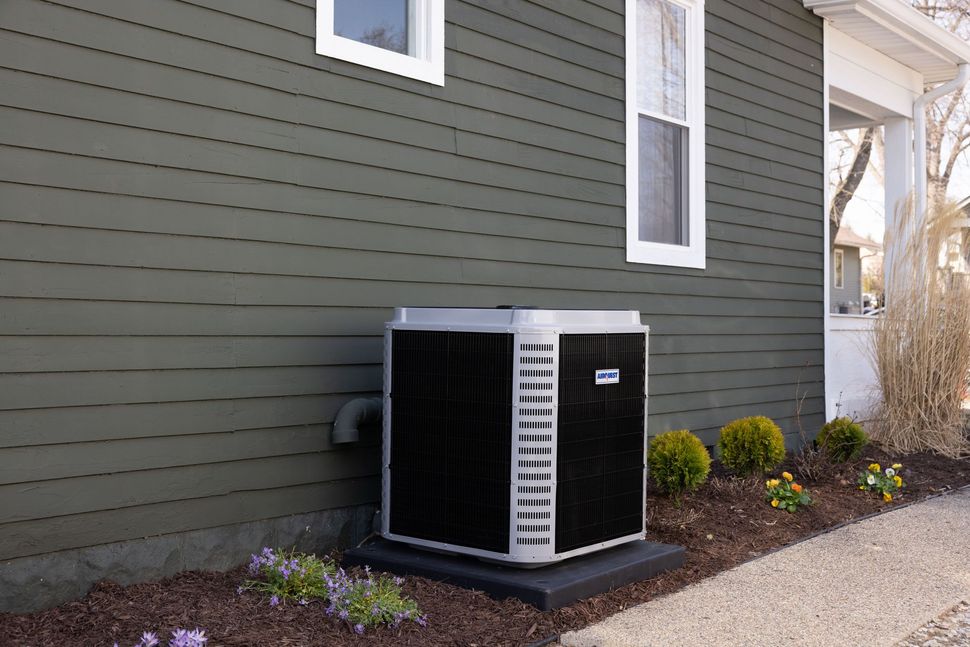 Air conditioner unit outside a house with dark green siding.
