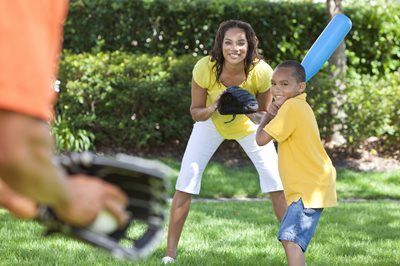 Woman and child playing backyard baseball, smiling as a blue bat swings at a ball.