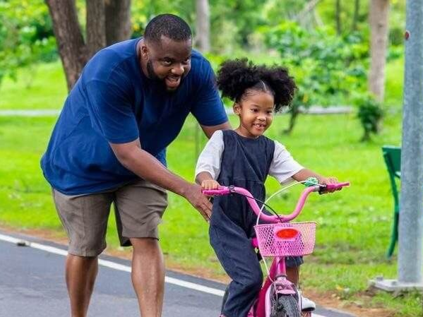 Man and child riding a pink bike together on a park path, smiling outdoors