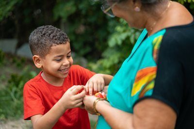 Child smiling while fastening a bracelet on an adult’s wrist outdoors