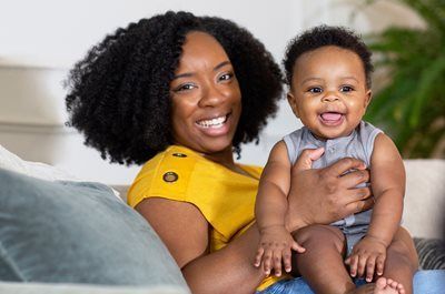 Smiling woman in a yellow top holding a laughing baby on a sofa