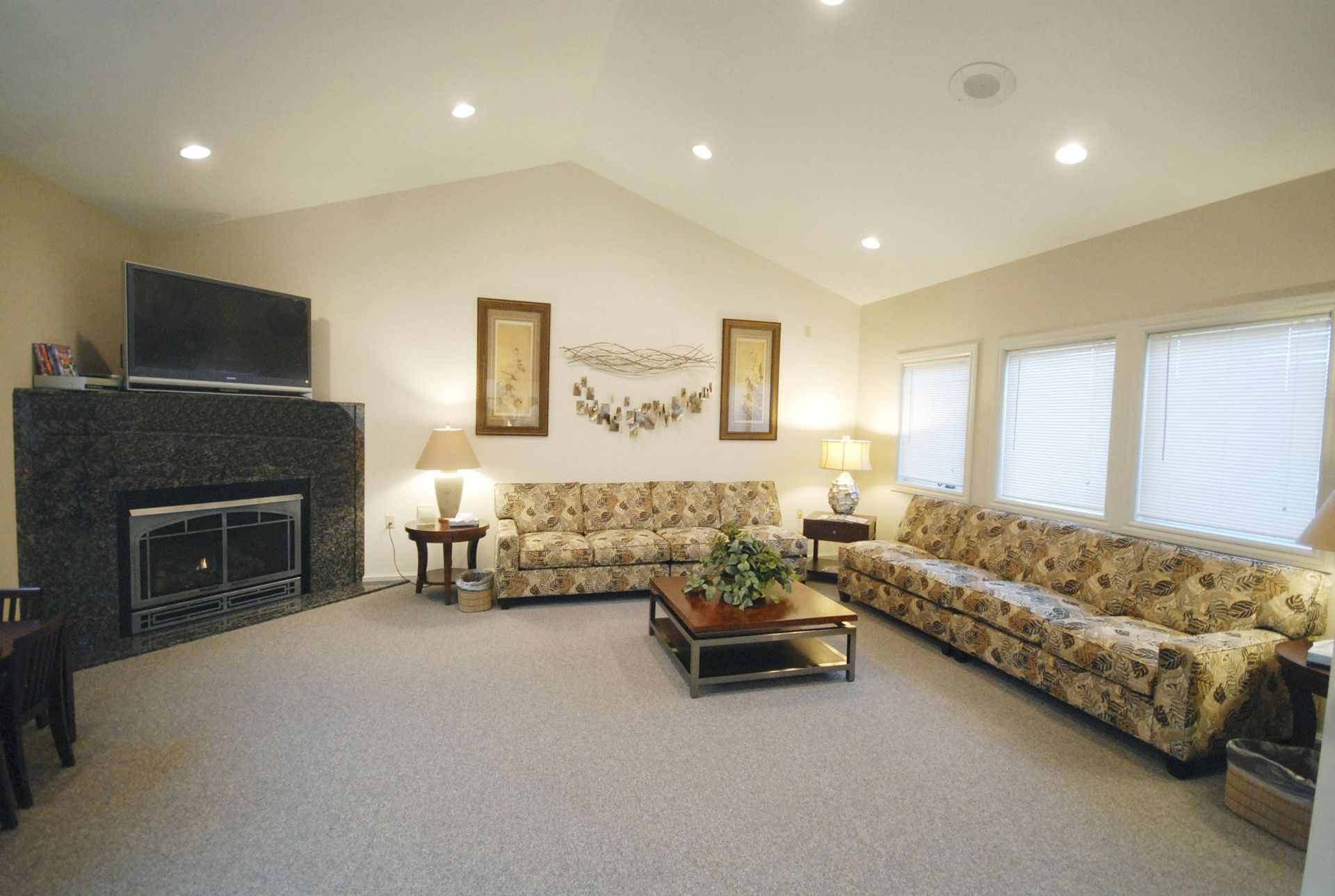 Cozy living room with stone fireplace, floral sofa, and large windows with blinds