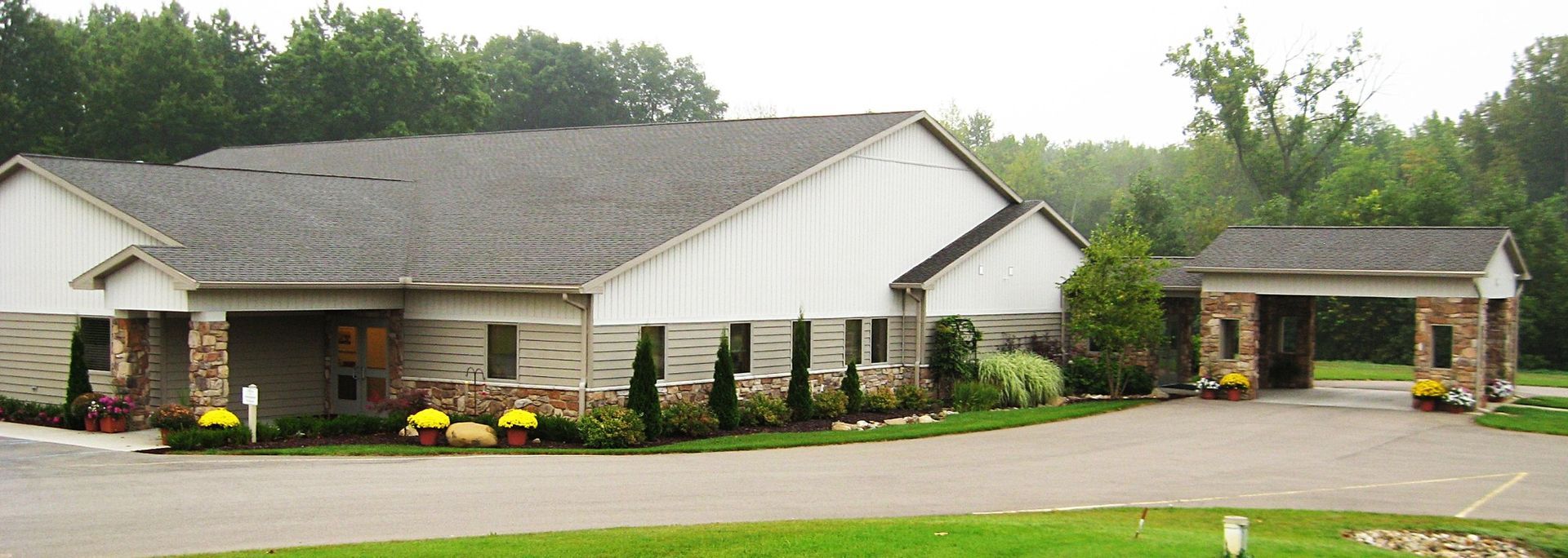 Single-story building with white siding, stone columns, and a small covered entrance beside a detached garage.