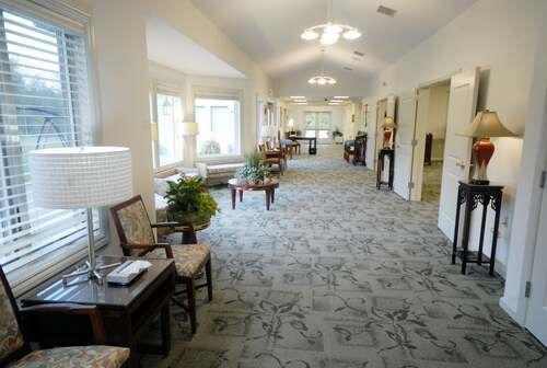 Bright hallway in a care facility with chairs, lamps, windows, and patterned carpet