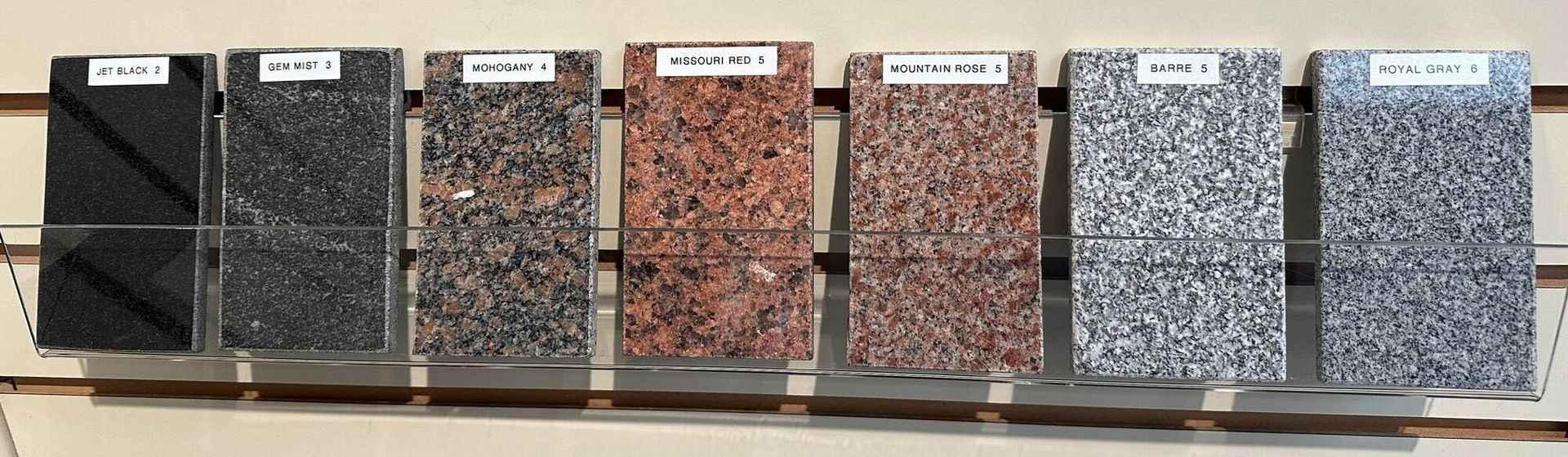 Six samples of speckled stone tiles in gray, black, brown, and blue displayed in a row