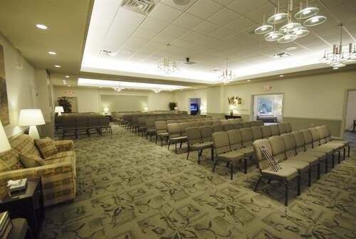 Empty conference room with rows of chairs, carpeted floor, and ceiling lights on beige walls
