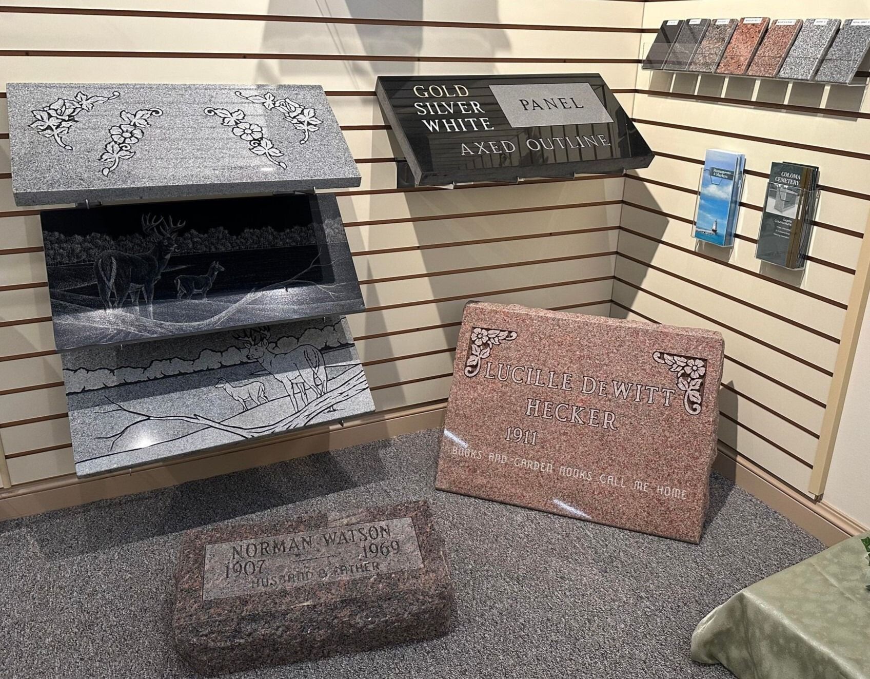 Display of assorted engraved stone memorial samples in a showroom, including gray, black, and pink pieces.