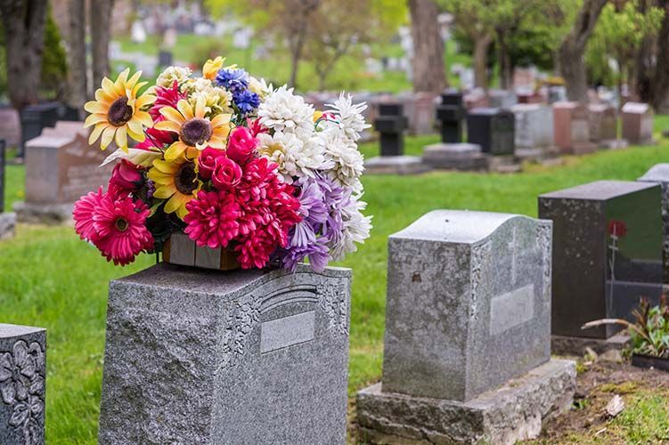Flower bouquet on a gravestone in a cemetery, with rows of gray headstones nearby.