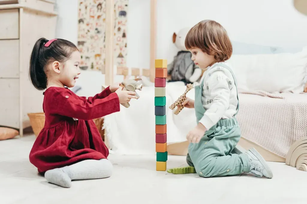 A toddler with blond hair sits on the floor playing with a wooden puzzle in a living room.