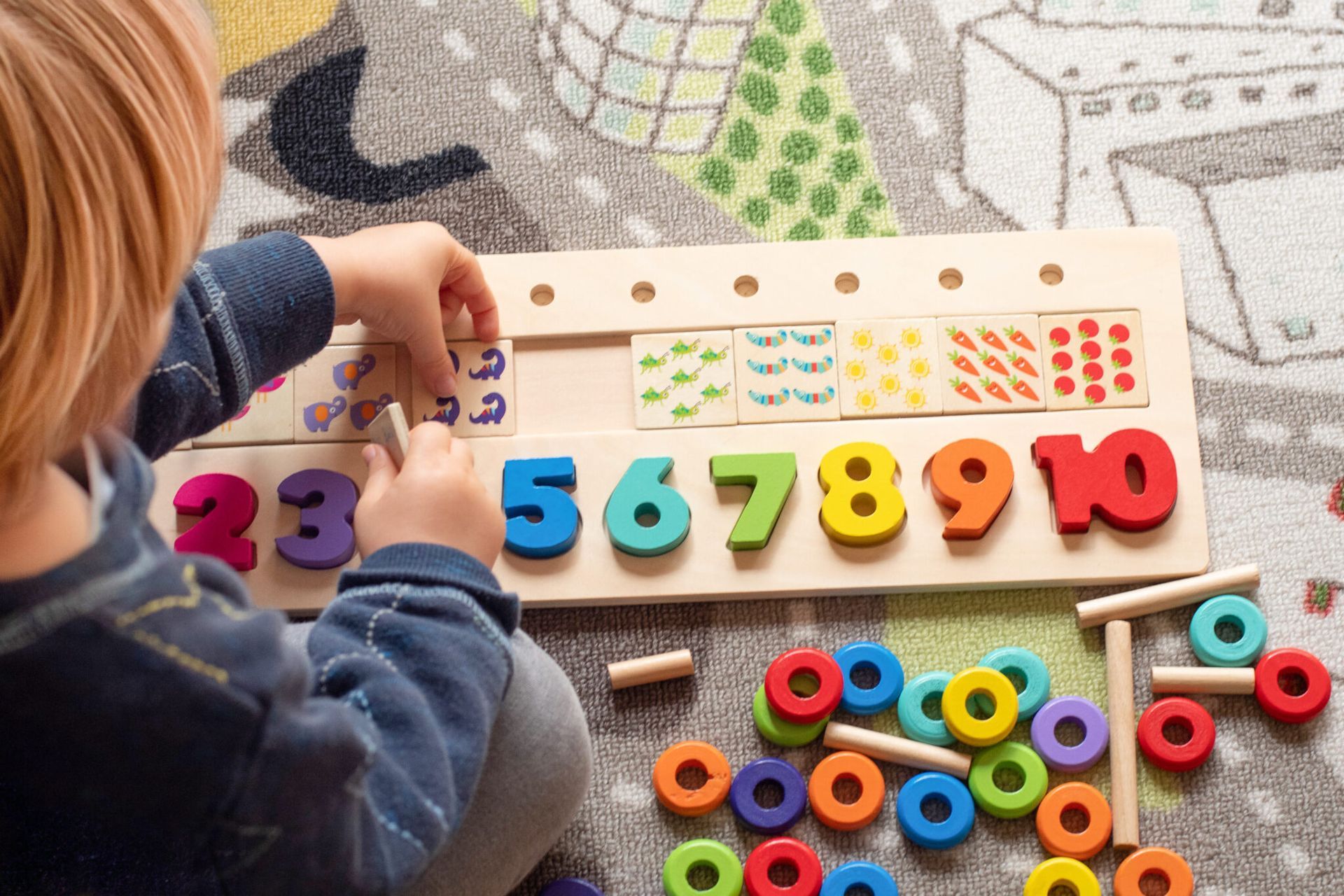 Boy playing with a puzzle with colorful numbers that go up to ten on a car rug. 