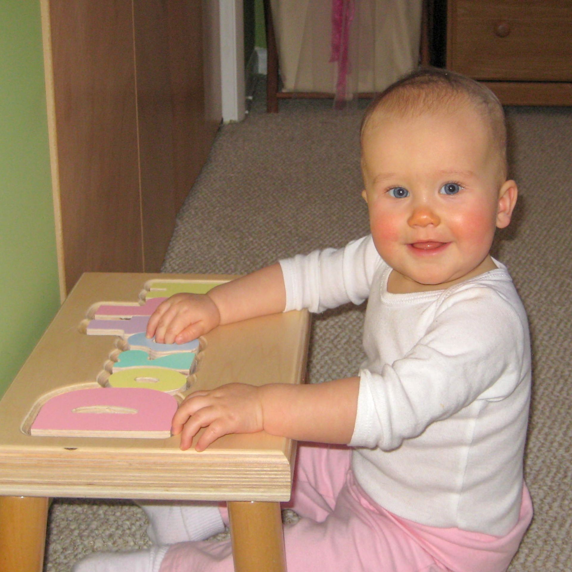 A baby smiling at the camera playing with her custom puzzle stool from Hollow Woodworks. 