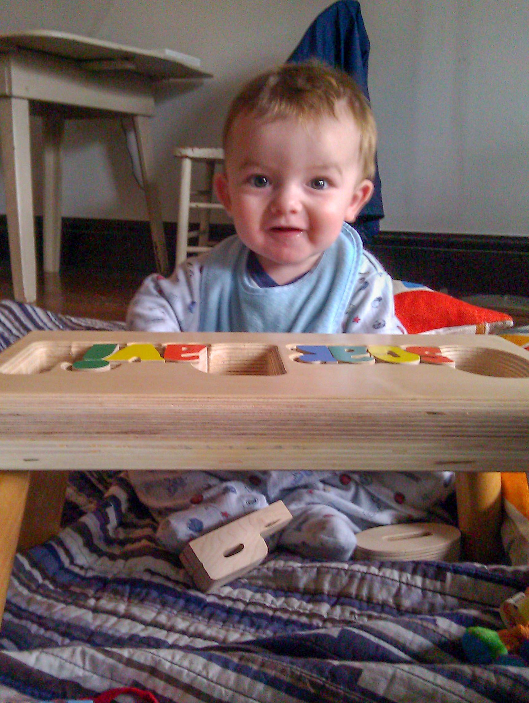 Smiling baby sitting behind a wooden toy xylophone on a striped blanket indoors