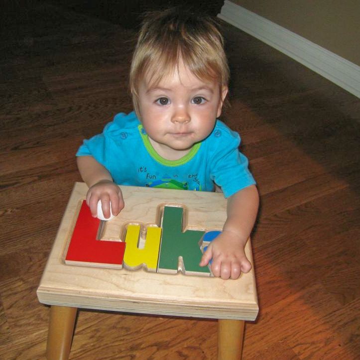 Toddler on a wooden floor playing with colorful alphabet block on a puzzle stool. 