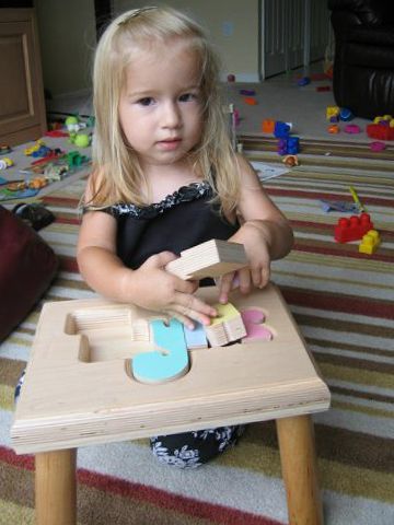 Child sitting on the floor, playing with wooden blocks at with a small puzzle stool. 