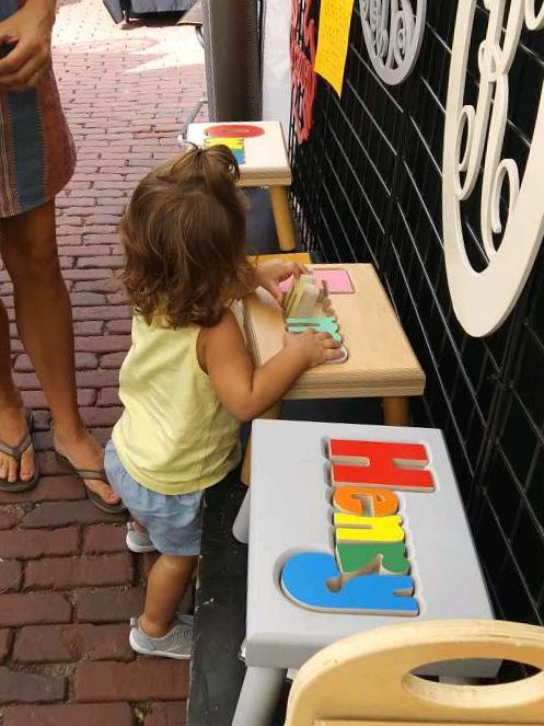A girl interacting with a maple puzzle stool at a hollow woodworks outdoor fair. 