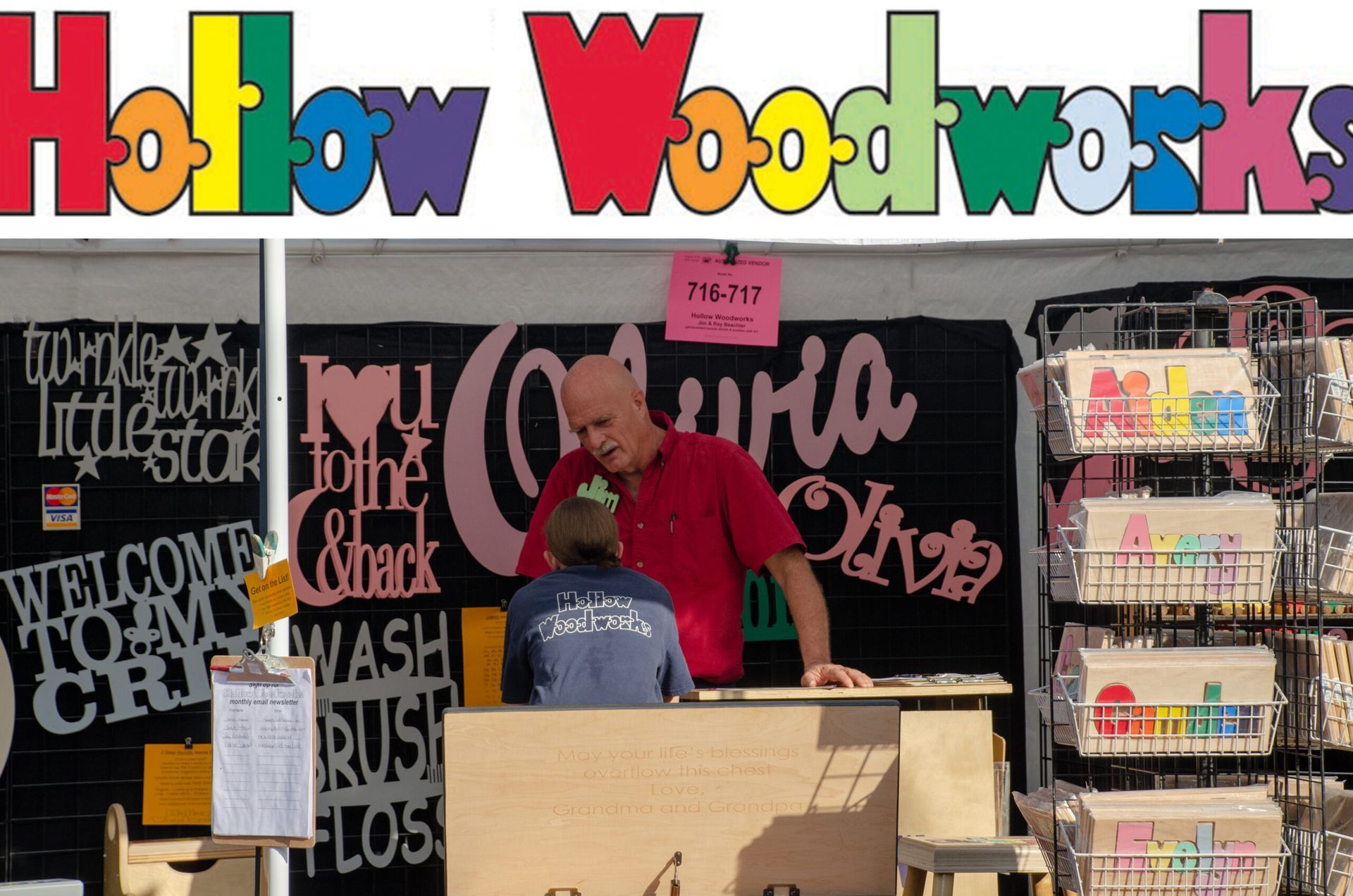 Hollow Woodworks booth with colorful sign, two people at a craft fair, and wood products on display