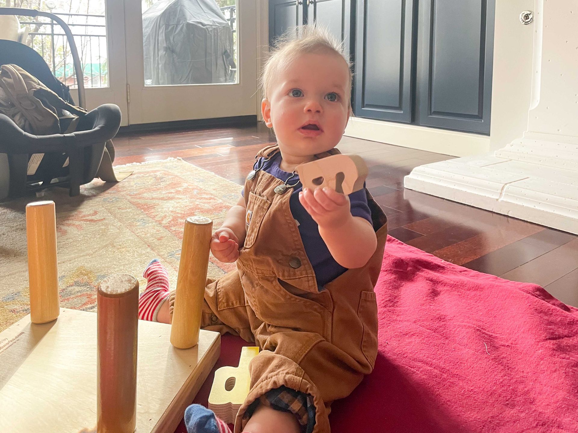 Baby on the ground playing with a puzzle piece off of the puzzle name stool that is flipped upside down.
