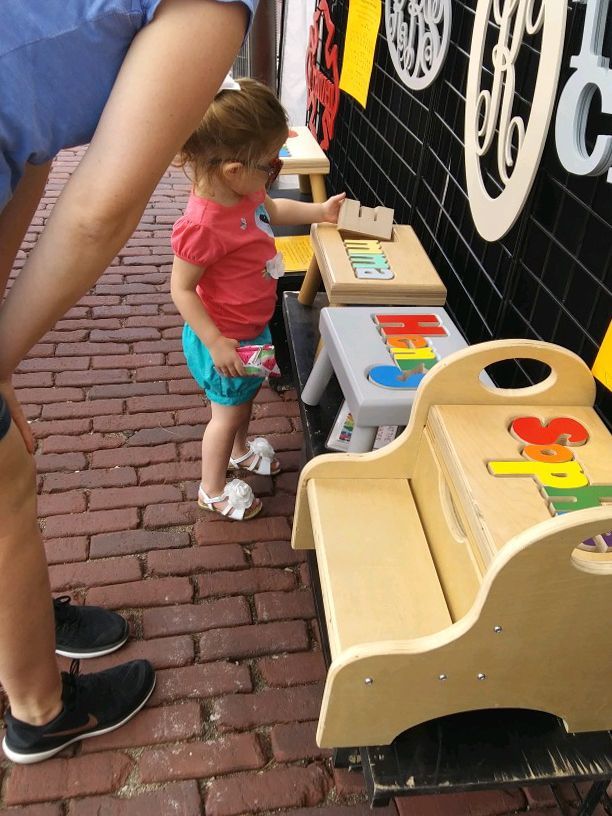 Toddler in pink shirt playing with colorful toys at an outdoor activity station on a brick walkway