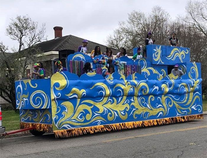 Blue parade float with gold swirls, people onboard.