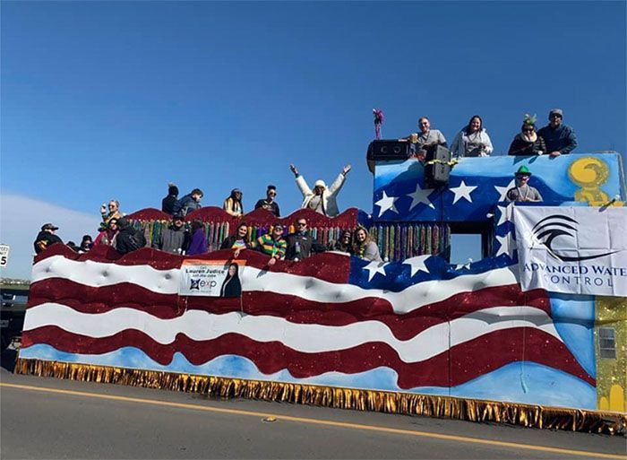Float decorated as American flag with people waving on board. Blue sky background.