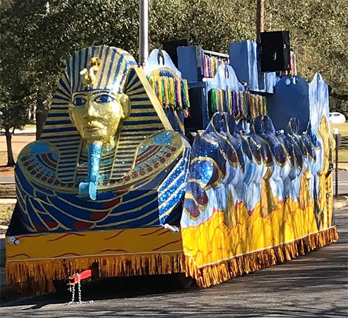 Mardi Gras float with a large golden pharaoh's bust. Blue, yellow, and gold decorations.