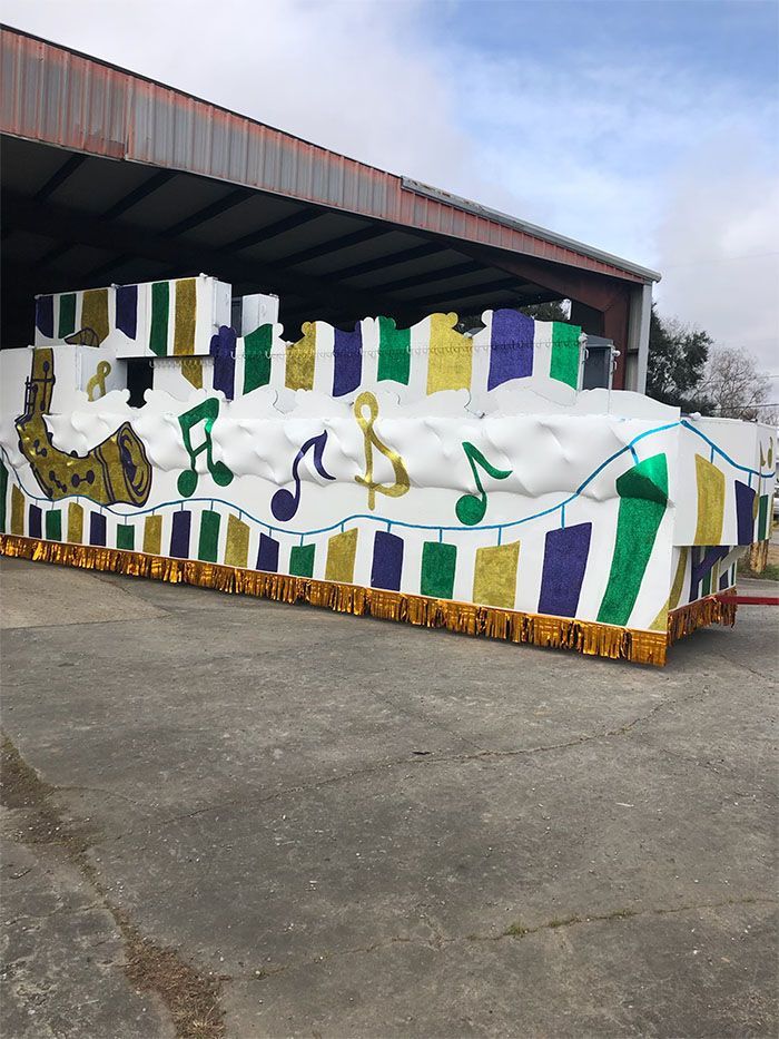 Mardi Gras parade float with gold, purple, and green decor.  Features a horn, musical notes, and castle-like structures.