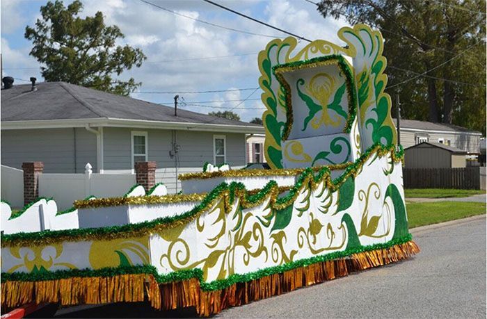 Mardi Gras parade float, white with gold and green accents, decorated with filigree and tinsel.