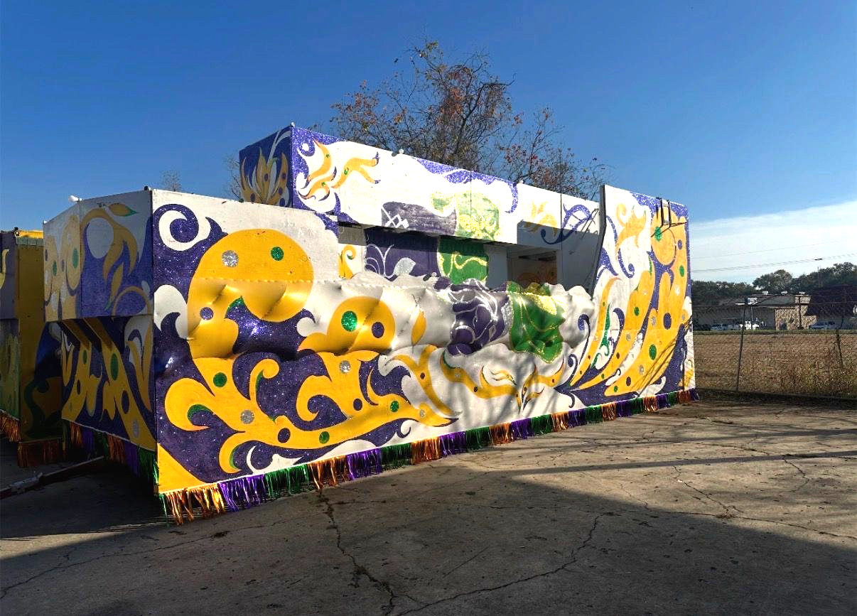 Mardi Gras float with purple, gold, and green decorations on a sunny day.