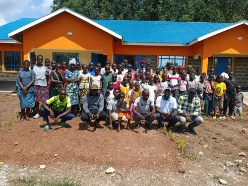 Group of people in front of an orange building with blue roof. Some are kneeling, smiling.