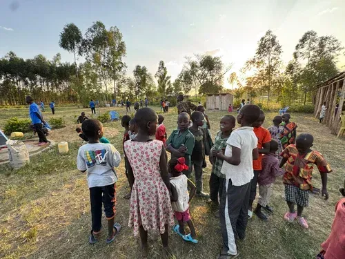Children gathered outdoors at sunset, looking up, some wearing casual clothing.