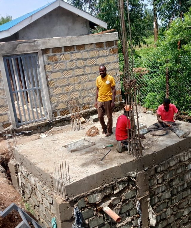 Workers building a concrete foundation beside a small brick house in a rural area
