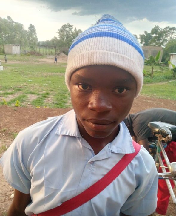 Young person wearing a blue and white knit hat, blue shirt, and red strap; outdoors.
